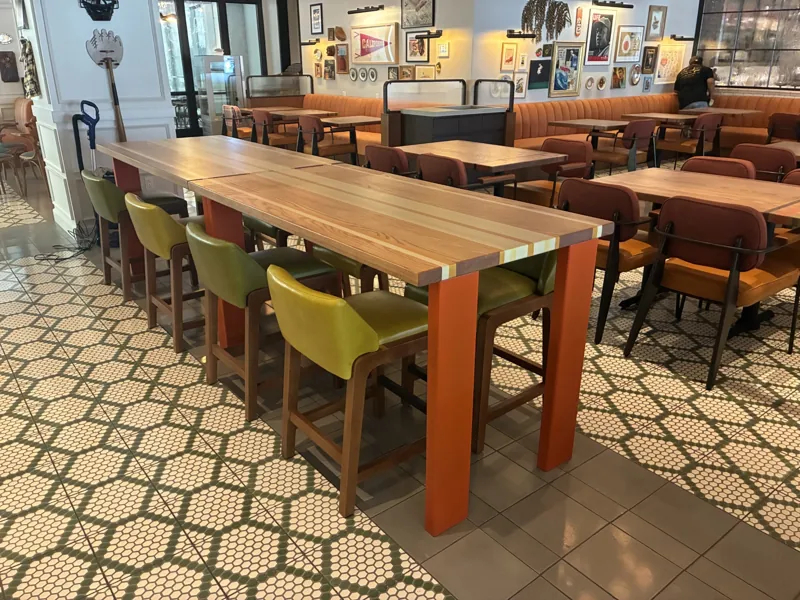 A long shared table with green stools, surrounded by the dining area at Birdie G's.