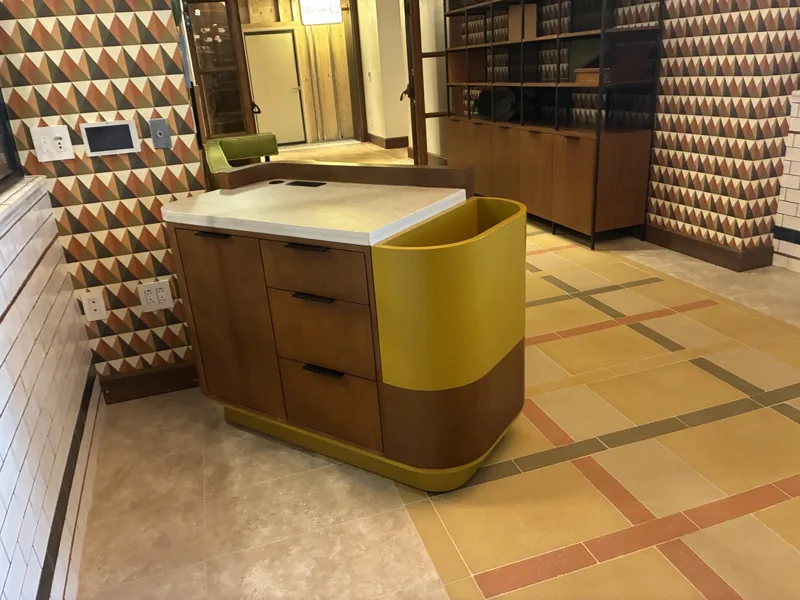 A curved welcome counter with a yellow accent beside display cabinetry at Birdie G's.