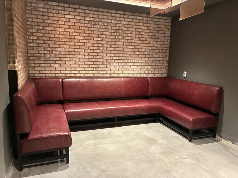 Burgundy upholstered seating follows the corner of a brick-lined space.