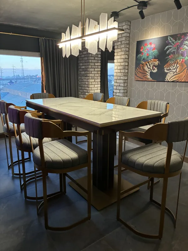 A table with upholstered metal barstools beneath a sculptural light fixture.